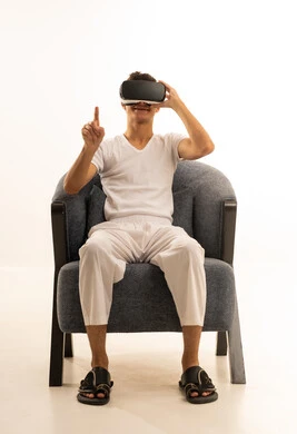 استخدام الأجهزة التقنية الحديثة, محاكاة العالم الخيالي, ارتداء نظارات الواقع الافتراضي,بورتريه لرجل عربي خليجي سعودي يرتدي السروال والفانيله البيضاء يجلس على كرسي مريح يضع نظارة الفي ار ثلاثية الأبعاد، قضاء وقت ممتع باللعب في العاب الفيديو ، خلفية بيضاء