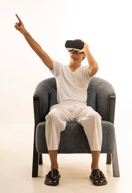 Simulation of the imaginary world, wearing virtual reality glasses, using modern technological devices, a portrait of a Saudi Arabian Gulf man wearing white pants and a t-shirt sitting on a comfortable chair wearing 3D VR glasses, having a good time playing video games, white background.
