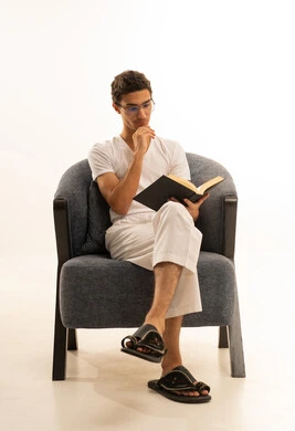 ثقافة التعلم الذاتي ، قراءة الكتب بتمعن، بورترية لرجل عربي خليجي سعودي يرتدي السروال والفانيله البيضاء يجلس على كرسي  مريح يمسك بيده كتاب تثقيفي ، الاستمتاع بقراءة الروايات والقصص، خلفية بيضاء