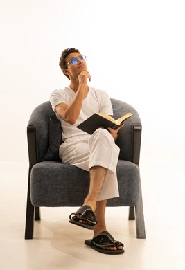 قراءة الكتب بتمعن، ثقافة التعلم الذاتي ، بورترية لرجل عربي خليجي سعودي يرتدي السروال والفانيله البيضاء يجلس على كرسي  مريح يمسك بيده كتاب تثقيفي ، الاستمتاع بقراءة الروايات والقصص، خلفية بيضاء