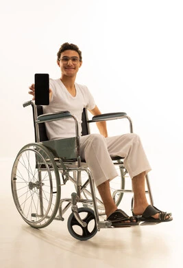 عرض شاشة سوداء فارغة عبر الجوال، ايماءات الفرح والسعادة، بورتريه لرجل عربي خليجي سعودي يرتدي السروال والفانيله البيضاء يجلس على كرسي متحرك يمسك بيده الهاتف المحمول، قضاء وقت ممتع في المنزل، استخدام جهاز تقني حديث ومتطور، خلفية بيضاء