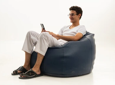 Chatting with friends and relatives via mobile, gestures of joy and happiness, a portrait of a Saudi Arabian Gulf man wearing pants and a white t-shirt sitting on a comfortable chair holding a mobile phone, enjoying time at home, using a modern and advanced technological device, white background.
