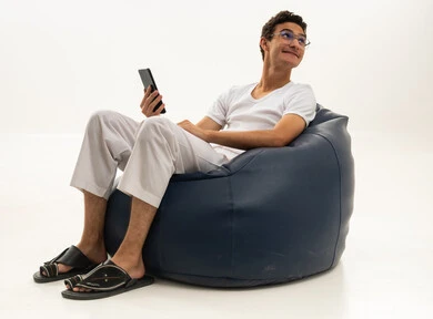 Gestures of joy and happiness, chatting with friends and relatives via mobile, a portrait of a Saudi Arabian Gulf man wearing pants and a white t-shirt sitting on a comfortable chair holding a mobile phone, spending enjoyable time at home, using a modern and advanced technological device, white background.