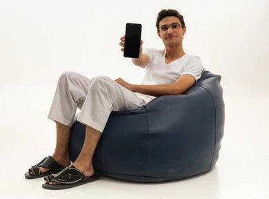 A display of a blank black screen, chatting with friends and relatives via mobile, a portrait of a Saudi Arabian Gulf man wearing white pants and a t-shirt sitting on a comfortable chair holding a mobile phone, enjoying time at home, using a modern and advanced technological device, white background.