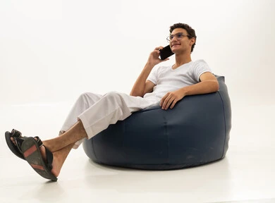 Chatting with friends and relatives via mobile, gestures of joy and happiness, a portrait of a Saudi Arabian Gulf man wearing pants and a white t-shirt sitting on a comfortable chair holding a mobile phone, enjoying time at home, using a modern and advanced technological device, white background.