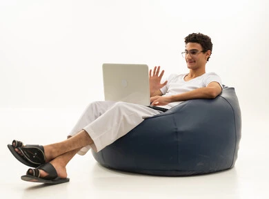 The use of modern and advanced devices, remote business management, a portrait of a Saudi Arabian Gulf man wearing pants and a white t-shirt sitting on a comfortable chair using a laptop, integrating technology with work, completing required tasks via the laptop, Saudi professions and jobs, white background.