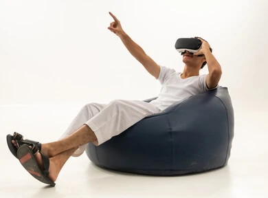 Wearing virtual reality glasses, simulating the imaginary world, using modern technological devices, a portrait of an Arab Gulf Saudi man wearing white pants and a t-shirt sitting on a comfortable chair wearing 3D VR glasses, having a good time playing video games, white background.