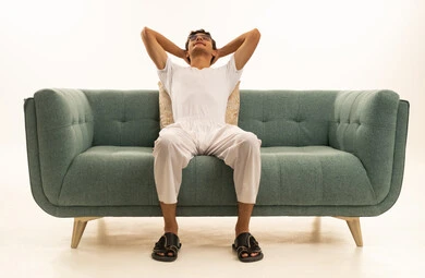 أخذ قسط من الراحة, ايماءات التأمل و الاستمتاع بوقت الهدوء, بورتريه لرجل عربي خليجي سعودي يرتدي السروال والفانيله البيضاء يجلس على اريكة مريحة يضع يديه خلف رأسه بتعابير الاسترخاء , خلفية بيضاء