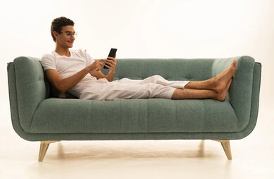 Chatting with friends and relatives via mobile, documenting memorable moments, a portrait of a Saudi Arabian Gulf man wearing pants and a white t-shirt sitting on a comfortable sofa holding a mobile phone, enjoying time at home, using a modern and advanced technological device, white background.