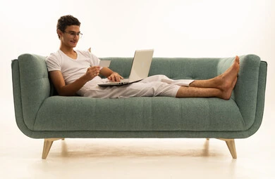 ادارة الأعمال عن بعد، استخدام الأجهزة الحديثة والمتطورة، بورتريه لرجل عربي خليجي سعودي يرتدي السروال والفانيله البيضاء يجلس على اريكة مريحة يقوم باستخدام الحاسوب المحمول، دمج التكنولوجيا بالعمل، إنجاز المهام المطلوبة عبر اللابتوب، مهن ووظائف سعودية ، خلفية بيضاء