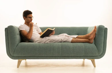 Expressions of thinking and contemplation, reading books attentively, the culture of self-learning, a portrait of a Saudi Arabian Gulf man wearing pants and a white t-shirt sitting on a comfortable sofa holding an educational book, enjoying reading novels and stories, white background.
