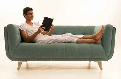 قراءة الكتب بتمعن، ثقافة التعلم الذاتي ، بورترية لرجل عربي خليجي سعودي يرتدي السروال والفانيله البيضاء يجلس على اريكة مريحة يمسك بيده كتاب تثقيفي ، الاستمتاع بقراءة الروايات والقصص، خلفية بيضاء