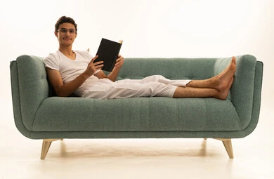Expressions of thinking and contemplation, reading books attentively, the culture of self-learning, a portrait of a Saudi Arabian Gulf man wearing pants and a white t-shirt sitting on a comfortable sofa holding an educational book, enjoying reading novels and stories, white background.