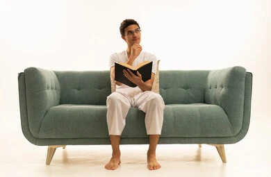 Reading books attentively, the culture of self-learning, a portrait of a Gulf Arab Saudi man wearing pants and a white t-shirt sitting on a comfortable sofa holding an educational book, enjoying reading novels and stories, white background.
