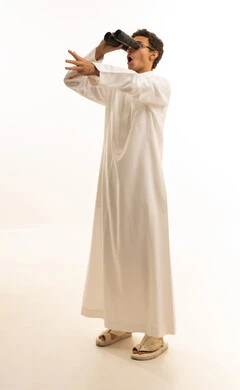 Seeing distant things through a telescope with gestures of amazement and joy, future planning for goals and ambitions, a portrait of a Saudi Arabian Gulf man wearing traditional attire looking through a binocular, a love for exploration and adventure, white background.