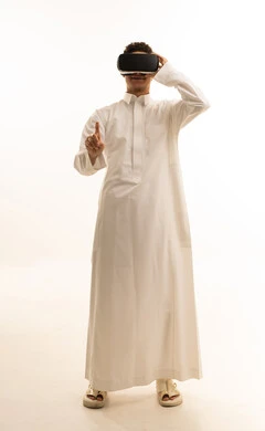 Using modern technical devices, simulating the imaginary world, wearing virtual reality glasses, a portrait of a Saudi Arabian Gulf man dressed in traditional attire wearing 3D VR glasses, having a good time playing video games, white background.
