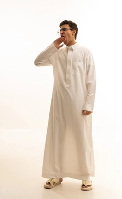 Expressions of drowsiness and the need for sleep, a portrait of a young Arab Gulf Saudi man with a dark complexion wearing a white thobe, raising his hands in gestures of drowsiness, the feeling of tiredness and yawning, the concept of laziness and lethargy, with a white background.