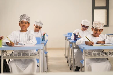 إنجاز الأعمال المدرسية، الإستعداد للعام الدراسي الجديد،العودة إلى المدارس، التعليم في سلطنة عمان، مجموعة من الطلاب العربيين الخليجيين العمانيين يرتدون الدشداشة والكمة يجلسون في مقاعدهم ويقومون بحل الواجب