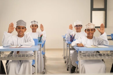 Gestures of enthusiasm to know the correct answer, participation and interaction within the classroom, Gulf Arab Omani students sitting in their seats raising their hands to answer, education and teaching with the prescribed curricula for students in the Sultanate of Oman.