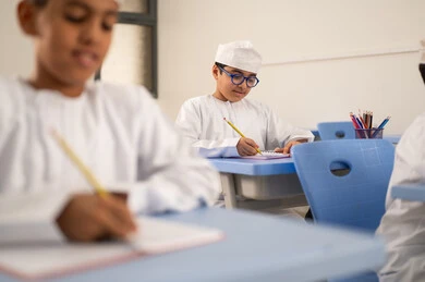 إنجاز التمارين الصفية، الإستعداد للعام الدراسي الجديد،العودة إلى المدارس، التعليم في سلطنة عمان، مجموعة من الطلاب العربيين الخليجيين العمانيين يرتدون الدشداشة والكمة يجلسون في مقاعدهم ويقومون بحل الواجب