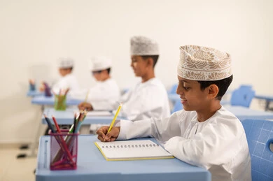 أداء الواجبات التعليمية ، الإستعداد للعام الدراسي الجديد،العودة إلى المدارس، التعليم في سلطنة عمان، مجموعة من الطلاب العربيين الخليجيين العمانيين يرتدون الدشداشة والكمة يجلسون في مقاعدهم ويقومون بحل الواجب
