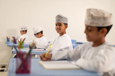 Completing the study exercises, preparing for the new school year, returning to school, education in the Sultanate of Oman, a group of Arab Gulf Omani students wearing the dishdasha and kumma are sitting in their seats and doing their homework.