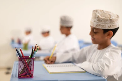 تنفيذ المهام المدرسية، الإستعداد للعام الدراسي الجديد،العودة إلى المدارس، التعليم في سلطنة عمان، مجموعة من الطلاب العربيين الخليجيين العمانيين يرتدون الدشداشة والكمة يجلسون في مقاعدهم ويقومون بحل الواجب