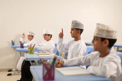 العودة إلى المدارس، تأدية الواجبات المدرسية، الإستعداد للعام الدراسي الجديد، التعليم في سلطنة عمان، مجموعة من الطلاب العربيين الخليجيين العمانيين يرتدون الدشداشة والكمة يجلسون في مقاعدهم ويقومون بحل الواجب