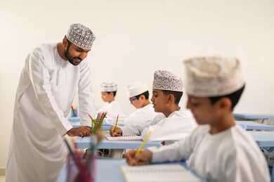 حوارات ودية بين الاستاذ والطلاب، التربية والتعليم بالمناهج المقررة للتلاميذ، جودة التعليم في سلطنة عمان، المشاركة الفعالة للطلاب مع المدرسين، معلم عربي خليجي عماني يرتدي الدشداشة والكمة يقوم بمناقشة الدروس مع طلابه