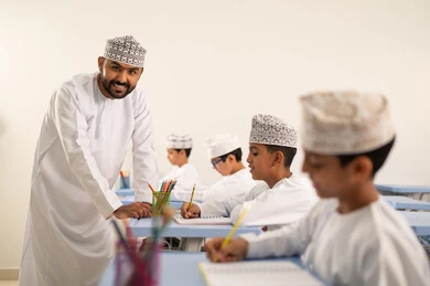 التربية والتعليم بالمناهج المقررة للتلاميذ، جودة التعليم في سلطنة عمان، المشاركة الفعالة للطلاب مع المدرسين، معلم عربي خليجي عماني يرتدي الدشداشة والكمة يقوم بمناقشة الدروس مع طلابه، حوارات ودية بين الاستاذ والطلاب