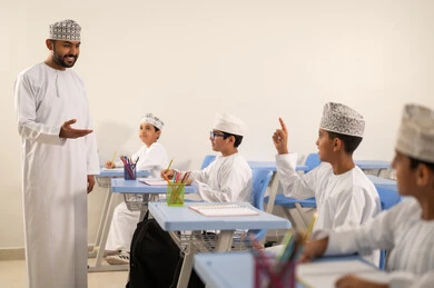 المشاركة الفعالة للطلاب مع المدرسين، معلم عربي خليجي عماني يرتدي الدشداشة والكمة يقوم بمناقشة الدروس مع طلابه، جودة التعليم في سلطنة عمان ، التربية والتعليم بالمناهج المقررة للتلاميذ، حوارات ودية بين الاستاذ والطلاب