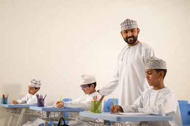 Preparation for the new school year, back to school, doing homework, education in the Sultanate of Oman, a group of Arab Gulf Omani students wearing the dishdasha and kumma sitting in their seats and doing their homework with their teacher.