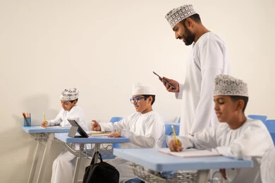 The use of digital tools in education, a Gulf Arab Omani teacher browsing the internet via a mobile phone, developed curricula and e-learning, the evolution of teaching methods in schools in the Sultanate of Oman, Gulf Arab Omani students sitting in their seats solving exam questions.