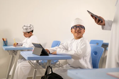 Benefiting from modern technologies and technology in learning and studying, a Gulf Arab Omani teacher is browsing the internet via a mobile phone, developed curricula and e-learning, the evolution of teaching methods in schools in the Sultanate of Oman, Gulf Arab Omani students sitting in their seats solving exam questions.