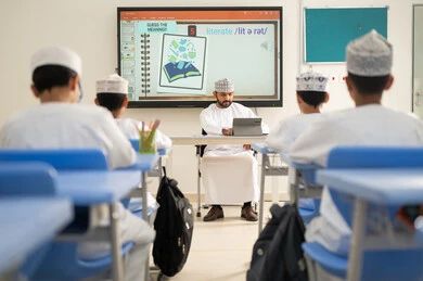 المشاركة الفعالة للطلاب، الاستفادة من التقنيات والتكنولوجيا الحديثة في التعلم والدراسة، المناهج المطورة والتعليم الالكتروني، تطور طرق التدريس في مدارس سلطنة عمان، طلاب عربيين خليجيين عمانيين يجلسون في مقاعدهم وأمامهم مدرس عماني يستخدم جهاز التابلت