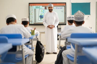 تشجيع الابتكار وتطوير القدرات العلمية، متابعة مجموعة من الطلاب داخل الفصل، معلم عربي خليجي عماني يرتدي الدشداشه والكمه يشرح لطلابه في بيئه مدرسيه تعليميه متطوره، نظام التعليم الحديث، جودة التعلم في المدارس الأكاديميه