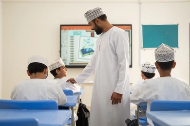 Developing sciences and stimulating creativity and skills, monitoring a group of students inside the classroom, an Arab Gulf Omani teacher wearing a dishdasha and kumma explaining to his students in an advanced educational school environment, modern education system, quality of learning in academic schools. Developing sciences and stimulating creativity and skills, monitoring a group of students inside the classroom, an Arab Gulf Omani teacher wearing a dishdasha and kumma explaining to his students in an advanced educational school environment, modern education system, quality of learning in academic schools.