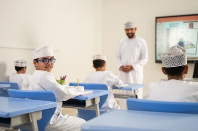 متابعة مجموعة من الطلاب داخل الفصل، معلم عربي خليجي عماني يرتدي الدشداشه والكمه يشرح لطلابه في بيئه مدرسيه تعليميه متطوره، نظام التعليم الحديث، تعزيز العلوم والإبتكارات وتنمية المهارات، جودة التعلم في المدارس الأكاديميه