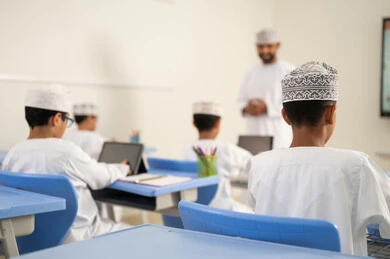 التعليم ودوره في تنشيط القدرات العقلية, التعليم في سلطنه عمان, اكتساب المعرفة و الخبرات العلمية, مفهوم الاجتهاد والتفوق, معلم عربي خليجي عماني يرتدي الدشداشة و الكمة يقوم بشرح الدروس للطلاب داخل الفصل، استخدام التابلت فى الدراسة