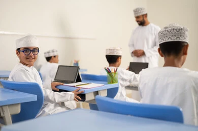 دور التعليم في تطوير التفكير وتنشيط القدرات الذهنية, التعليم في سلطنه عمان, اكتساب المعرفة و الخبرات العلمية, مفهوم الاجتهاد والتفوق, معلم عربي خليجي عماني يرتدي الدشداشة و الكمة يقوم بشرح الدروس للطلاب داخل الفصل، استخدام التابلت فى الدراسة