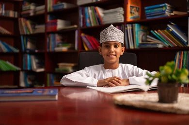 الاهتمام بتصفح الكتب المفيدة، قضاء وقت الفراغ بالتعلم والتثقف الذاتي، تنمية مهارة القراءة للطلاب، حب الثقافة والاستطلاع، طالب عربي خليجي عماني يرتدي الدشداشة و الكمة  يقوم بقراءة كتاب, زيارة مكتبة المدرسة، التعليم والدراسة في سلطنه عمان