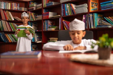 Love of culture and exploration, spending free time learning and self-education, visiting the school library, two Arab Gulf students from Oman wearing the dishdasha and kumma reading books, education and study in the Sultanate of Oman, developing reading skills for students, interest in browsing useful books.