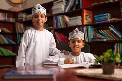 Collaborative work among students, solving educational exercises, education in the Sultanate of Oman, preparation for the new school year, back to school, two Arab Gulf Omanis wearing the dishdasha and kumma sitting inside the school library discussing lessons.