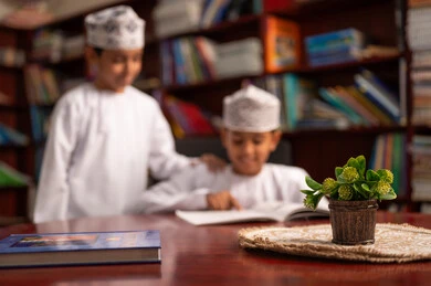العمل التشاركي بين الطلبة، حل التمارين التعليمية، التعليم في سلطنة عمان، الإستعداد للعام الدراسي الجديد، العودة إلى المدارس،البان عربيان خليجيان عمانيان يرتديان الدشداشة و الكمة يجلسان داخل المكتبة المدرسية يقومون بمناقشة الدروس