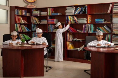 تنمية مهارة القراءة للطلاب، حب الثقافة والاستطلاع، مجموعه من الطلاب العربيون الخليجيون العمانيون يرتدون الدشداشة والكمة يجلسون داخل المكتبة المدرسية، التعليم والدراسة في سلطنة عمان ، قضاء وقت الفراغ بالتعلم والتثقف الذاتي، حل الواجبات المدرسية