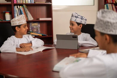 حل التمارين والفروض الصفية، مفهوم الاجتهاد وطلب التفوق، أهمية العلم في تنمية القدرات العقلية، التربية والتعليم في سلطنه عمان، مجموعه من الطلاب العربيون الخليجيون العمانيون يرتدون الدشداشة والكمة يجلسون داخل مكتبه المدرسة، استخدام التابلت فى الدراسة