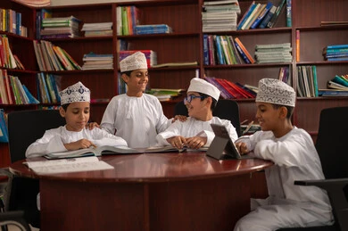 Completing daily study tasks, the concept of diligence and the pursuit of excellence, the importance of knowledge in developing mental abilities, education in the Sultanate of Oman, a group of Arab Gulf Omani students wearing the dishdasha and kumma sitting inside the school office, using tablets in studying.