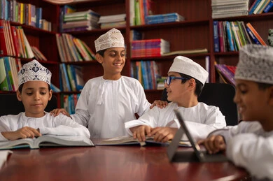 إنجاز الواجبات المدرسية، مفهوم الاجتهاد وطلب التفوق، أهمية العلم في تنمية القدرات العقلية، التربية والتعليم في سلطنه عمان، مجموعه من الطلاب العربيون الخليجيون العمانيون يرتدون الدشداشة والكمة يجلسون داخل مكتبه المدرسة، استخدام التابلت فى الدراسة