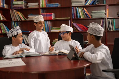 Homework solutions, the concept of diligence and the pursuit of excellence, the importance of knowledge in developing mental abilities, education in the Sultanate of Oman, a group of Arab Gulf students from Oman wearing the dishdasha and kumma sitting inside the school office, the use of tablets in studying.