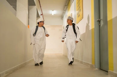 Developing relationships of familiarity and closeness among students, preparing for the new school semester, play and leisure time, two Gulf Arab students wearing the dishdasha and kumma and carrying school bags walking inside the school building, gestures of happiness and fun, academic schools in the Sultanate of Oman.